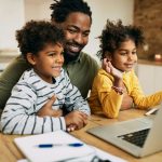 Happy black father and children having video call over laptop at home.